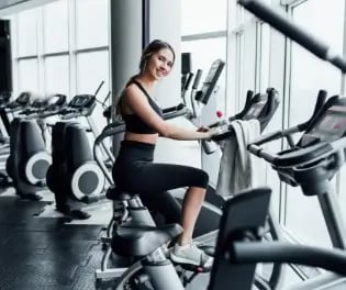 attractive-smiling-girl-onn-exercise-bike-modern-spacious-gym (1)