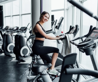 attractive-smiling-girl-onn-exercise-bike-modern-spacious-gym